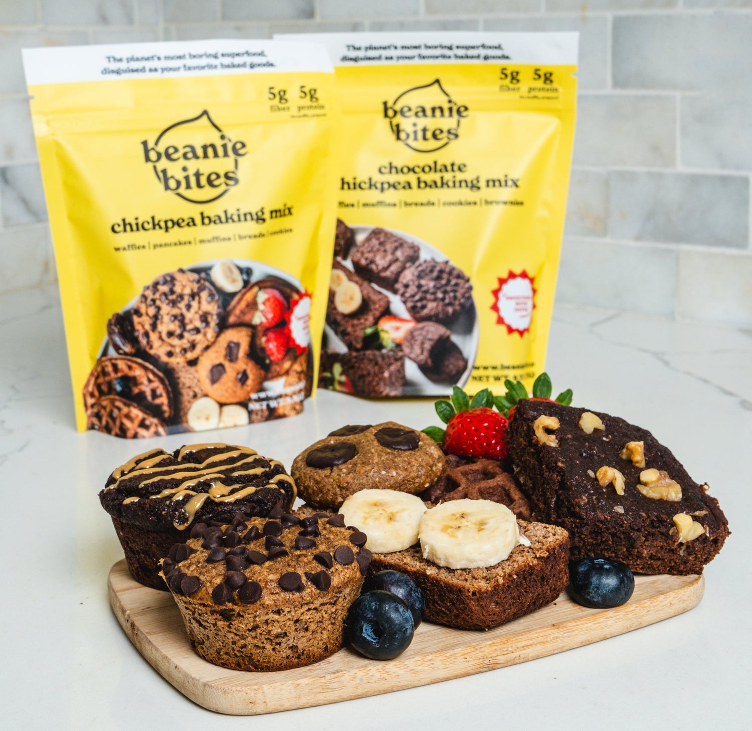 Beanie Bites baking mix packages with baked goods on a wooden board.

