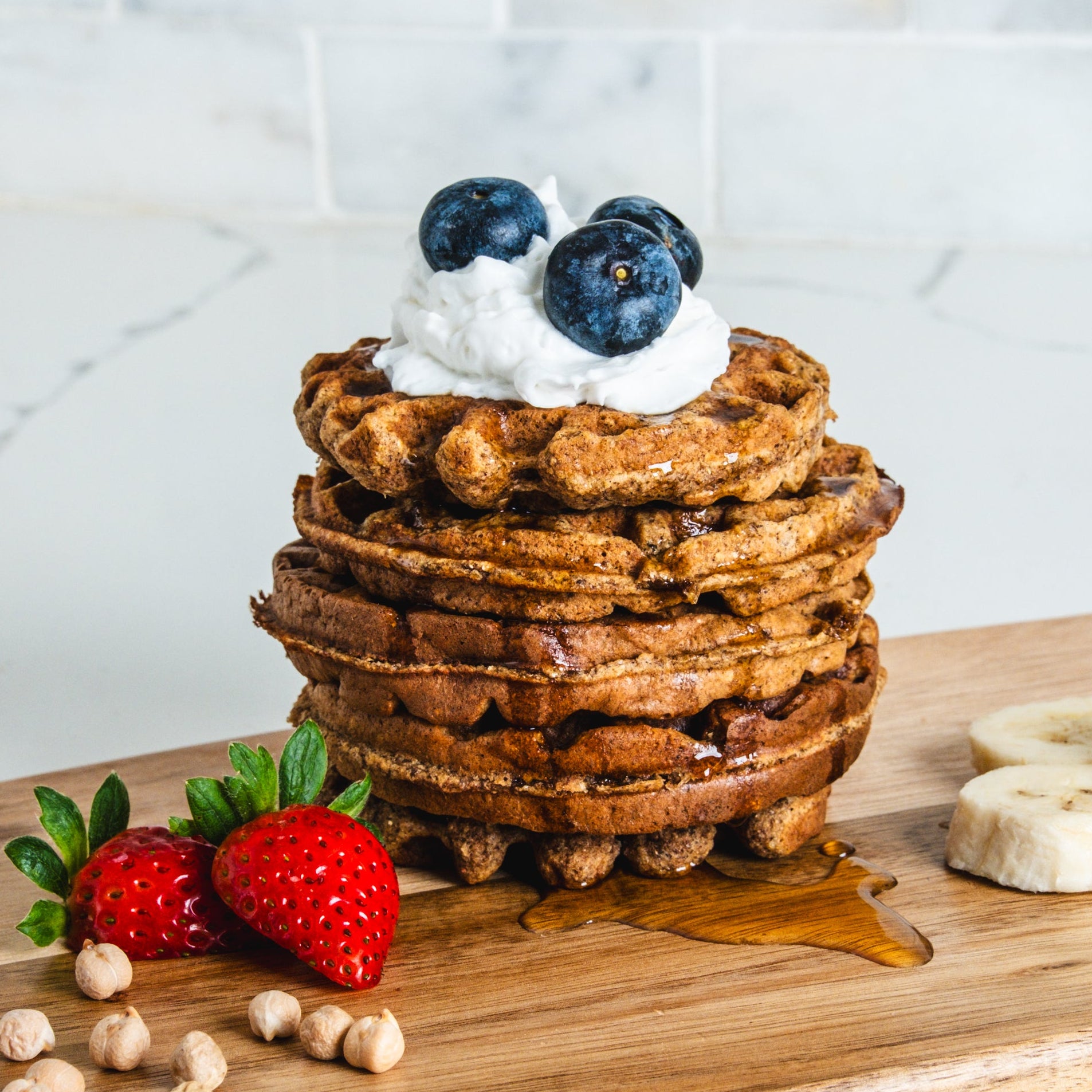 Stack of waffles with berries and whipped cream on a wooden board with a marble background

